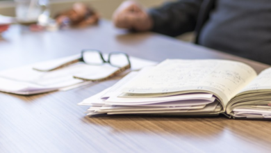 Imagen que muestra un cuaderno co apuntes, unos lentes de aumento y personas durante su descanso laboral